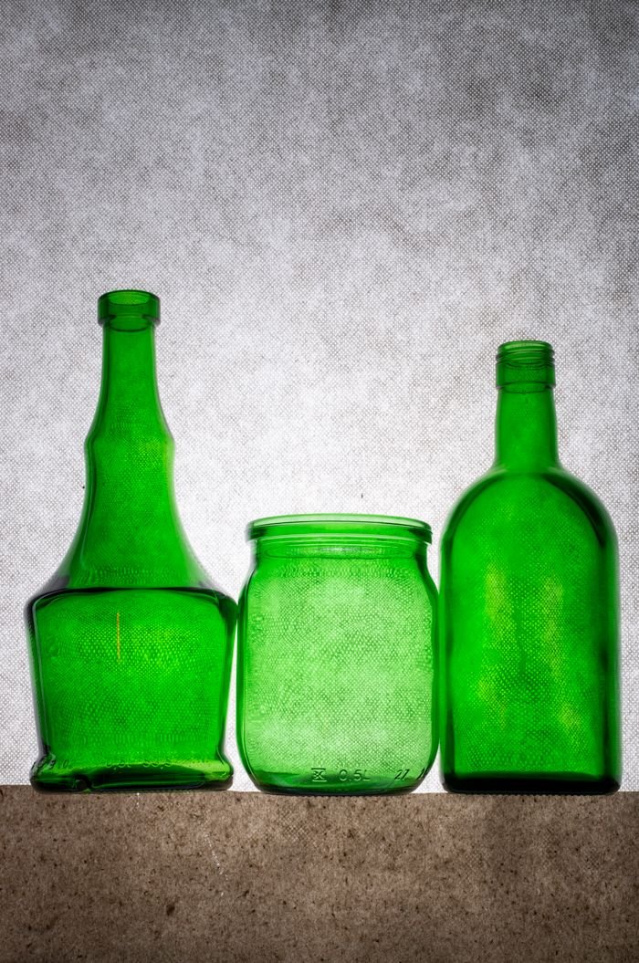 Three green glass bottles on a textured background, showcasing transparent design.