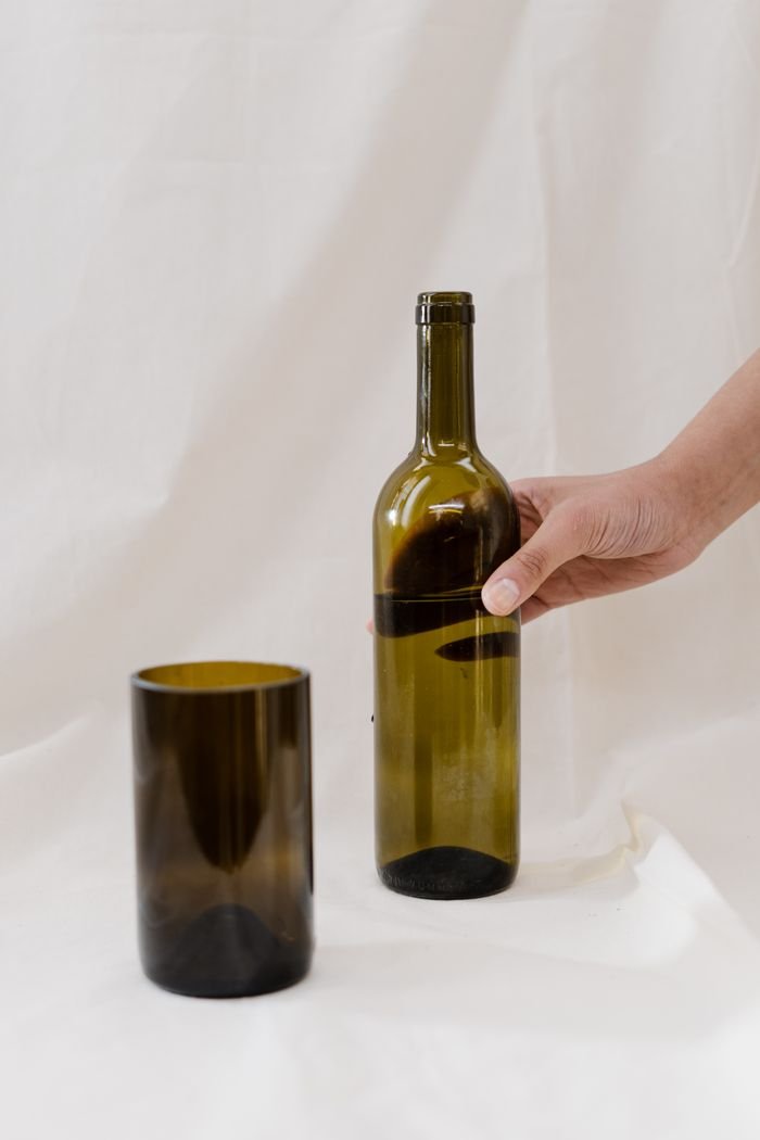 Eco-conscious person holding upcycled glass bottle and glass container on neutral background.